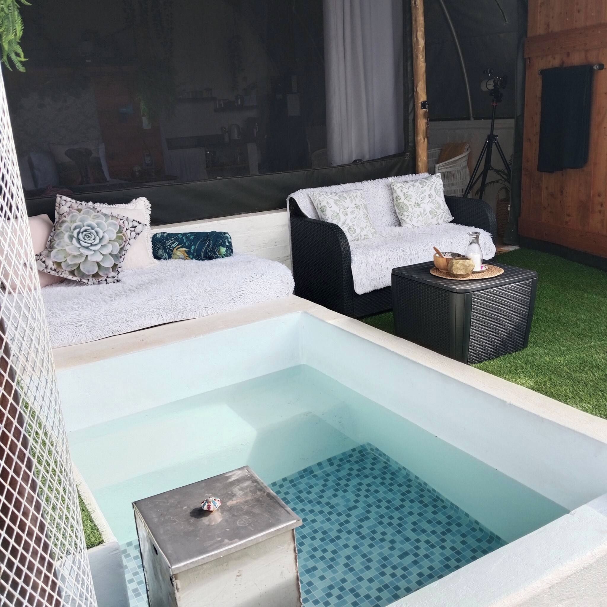 Ein Wellnessbereich mit Whirlpool, zwei Sofas mit gemusterten Kissen, einem kleinen Tisch mit Flasche und Schale sowie einem Fliesenboden.