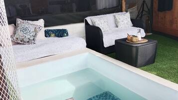 Ein Wellnessbereich mit Whirlpool, zwei Sofas mit gemusterten Kissen, einem kleinen Tisch mit Flasche und Schale sowie einem Fliesenboden.