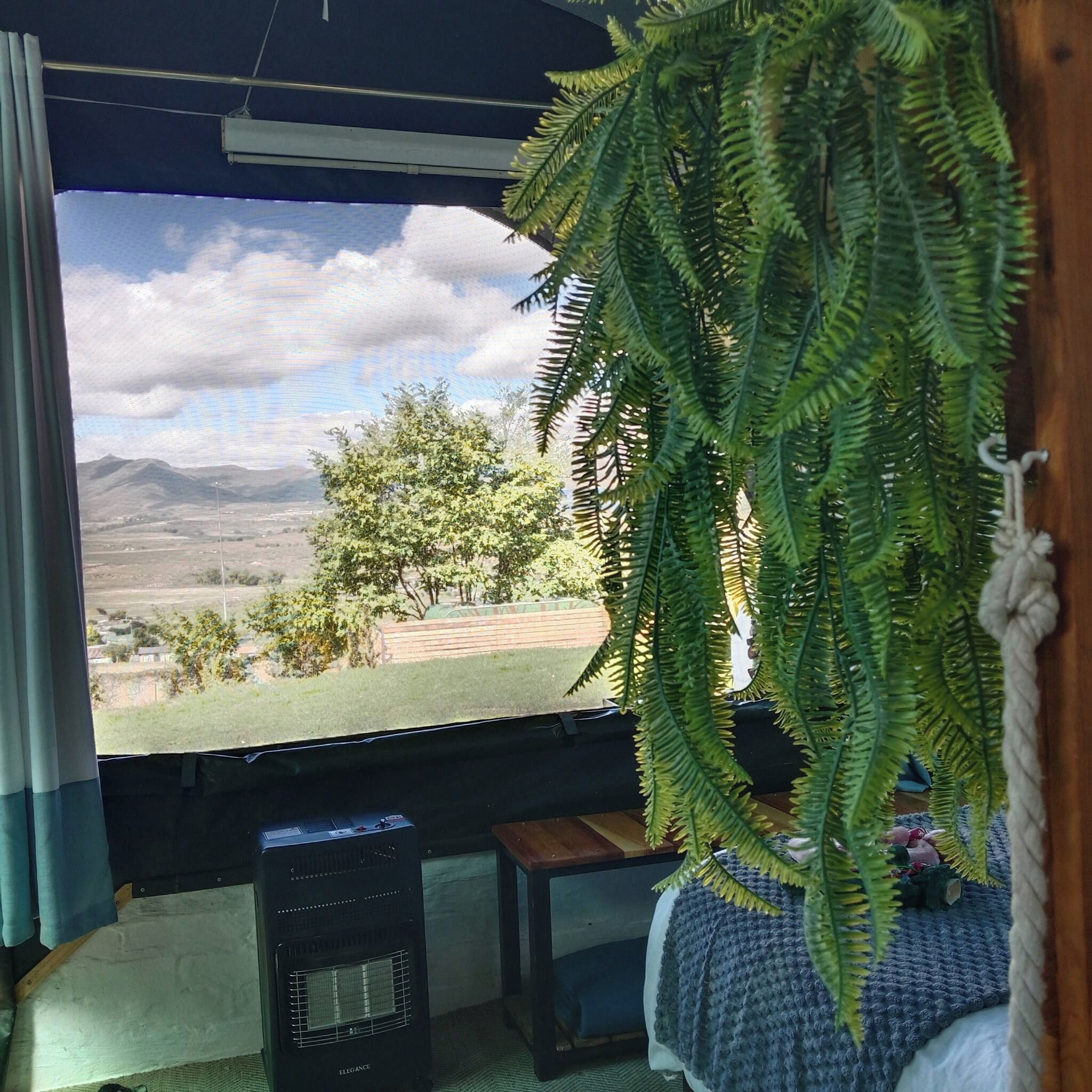 A room with a large window, a potted fern, a heater, and a small table.