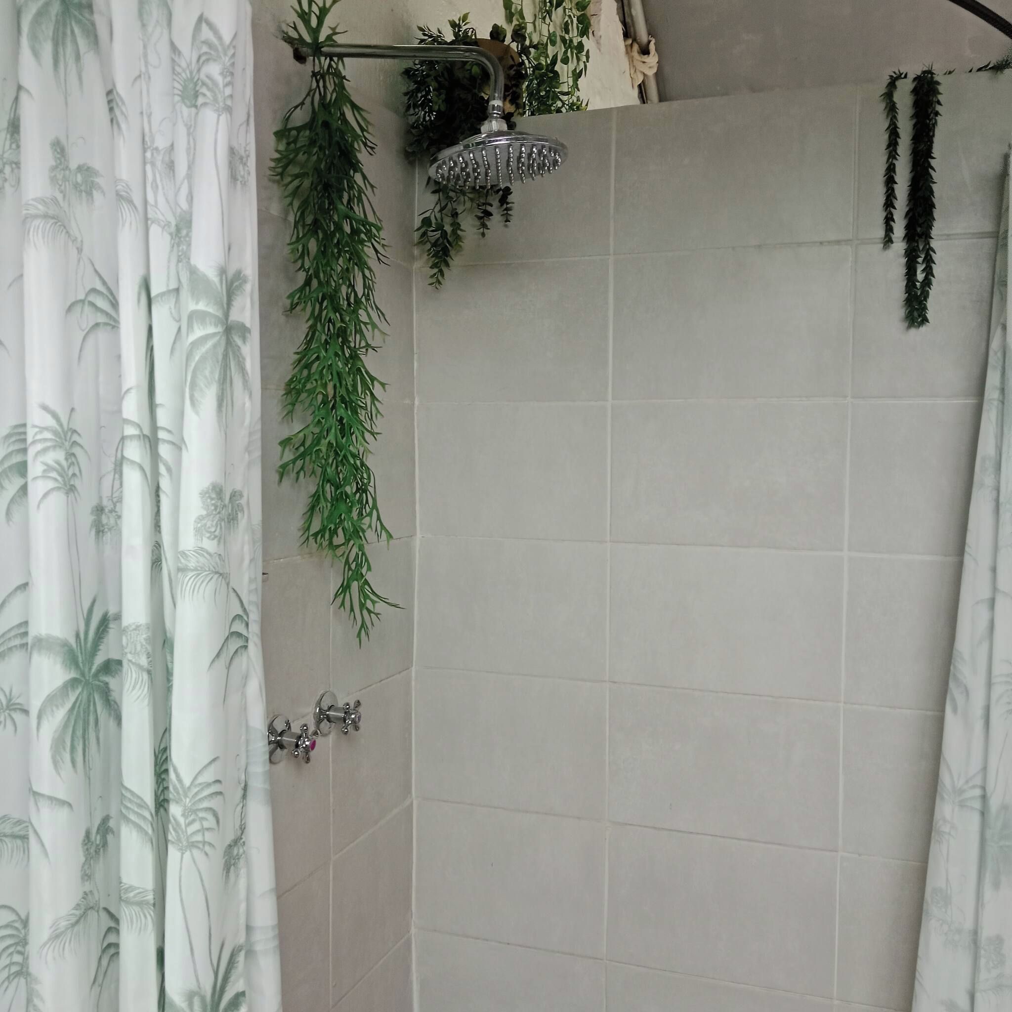 A bathroom with a shower, tiled walls, and a curtain with a palm tree pattern.