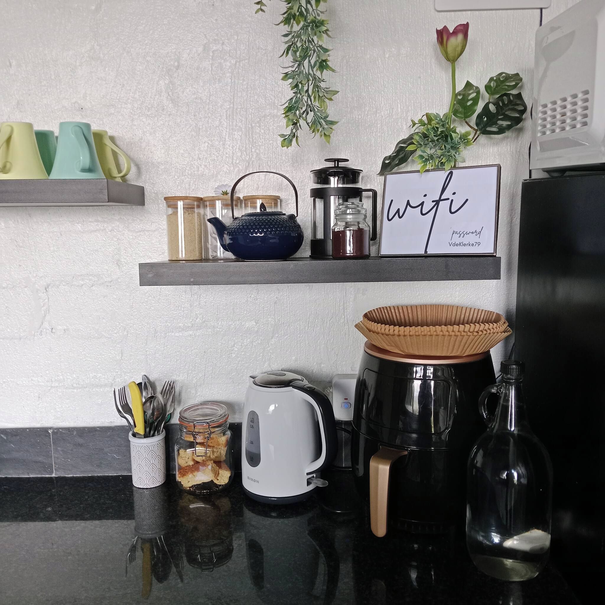 A kitchen counter with various appliances and items, including a coffee maker, a kettle, and a jar with utensils.