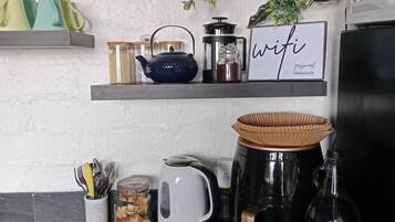 A kitchen counter with various appliances and items, including a coffee maker, a kettle, and a jar with utensils.