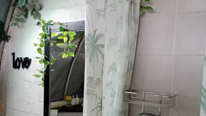 Et badeværelse med hvid vask, spejl, toilet, bruseforhæng med palmebladsmønster og et hyldesæt med toiletartikler.