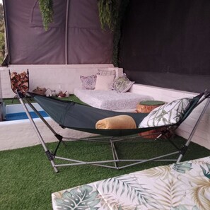 A hammock chair with a cushion, a small white sofa with patterned cushions, and a decorative plant.