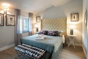 A bedroom with a large bed, a bedside table, a nightstand, a window with curtains, and framed pictures on the walls. - Villa Asti a luxury villa for enjoyment in Tuscany (Capannori)