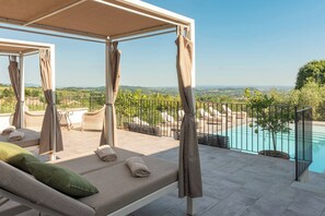 Un espace extérieur aménagé, baigné de soleil, avec une piscine, entouré d’une clôture en métal et offrant une vue sur un paysage.