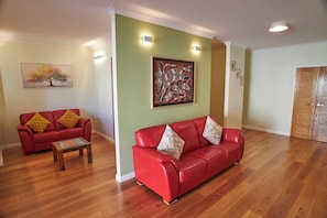 A living room with two red sofas, a wooden coffee table, and a painting on the wall.