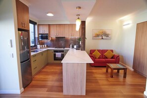 A modern kitchen with wooden cabinets, a central island, and a red sofa in a living area.