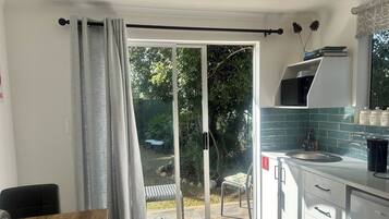 Una cocina moderna con microondas, lavamanos y armarios, un comedor con mesa y sillas, y un puerta corrediza de vidrio que da a un jardín.