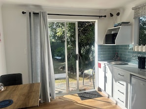 A modern kitchen with a microwave, sink, and cabinets, a dining area with a table and chairs, and a sliding glass door leading to a garden.