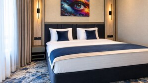 Habitación de hotel con una cama grande, cabecero, una obra de arte en la pared y suelo alfombrado.