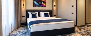 Habitació d'hotel amb un llit gran, un capçal de llit, una obra d'art penjada a la paret i un sòl amb moqueta.