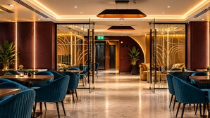 Un interior moderno con un pasillo central que conduce a una zona de recepción, flanqueado por áreas de descanso con mesas y sillas.