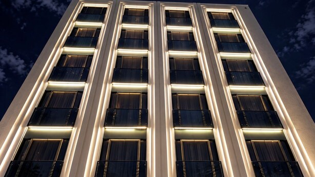 Un edificio de gran altura con varios pisos, que presenta un diseño arquitectónico moderno con ventanas iluminadas y fachada limpia.