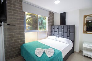 A hotel room with a bed, a window with a view of greenery, a white bedside table, and a mirror. - 21 Studio near the forest and Atanasio (Medellín)