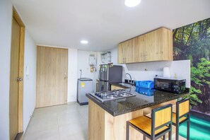 A compact kitchen with wooden cabinets, a gas stove, a refrigerator, and a microwave. - 21 Studio near the forest and Atanasio (Medellín)