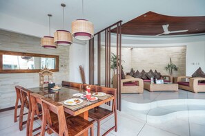 A modern dining area with a wooden table and chairs, a large mirror, and a ceiling fan. - K Villa Seminyak by Premier Hospitality  (Seminyak)