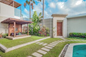 A modern outdoor area with a wooden pergola, a seating area, a swimming pool, and a variety of tropical plants. - K Villa Seminyak by Premier Hospitality  (Seminyak)