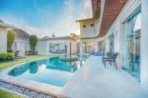 A modern outdoor swimming pool with a glass enclosure, surrounded by a patio area with seating and a view of a neighboring building. - K Villa Seminyak by Premier Hospitality  (Seminyak)