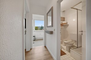 Ein Flur, der zu einem Badezimmer mit Toilette, Dusche und einem Fenster führt.