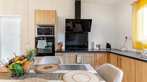 A modern kitchen with wooden cabinets, a built-in oven, microwave, and a black range hood. - Vrbo Property (Saint-Louis)