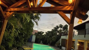 A covered outdoor area with a pool, wooden pergola, and surrounding vegetation. - Vrbo Property (Saint-Louis)