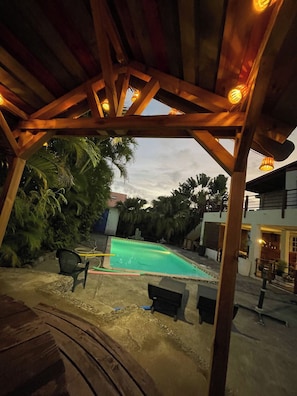 Un espace extérieur abrité comprenant une piscine, une pergola en bois et une végétation luxuriante.