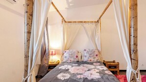 A four-poster bed with floral bedding, a bedside lamp, and a nightstand. - Vrbo Property (Saint-Louis)