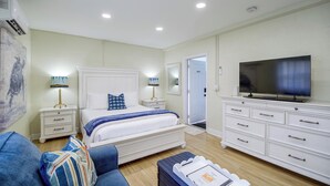 A modern bedroom with a bed, bedside tables, a dresser, a television, and a door leading to another room. - 1/2 Mi to Ocean! Couple's Haven in Satellite Beach (Satellite Beach)
