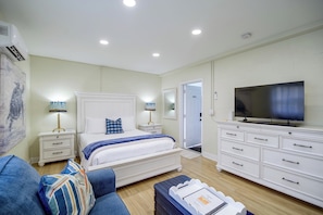 Quarto moderno com cama, mesas de cabeceira, cômoda, televisão e porta que dá para outro ambiente.