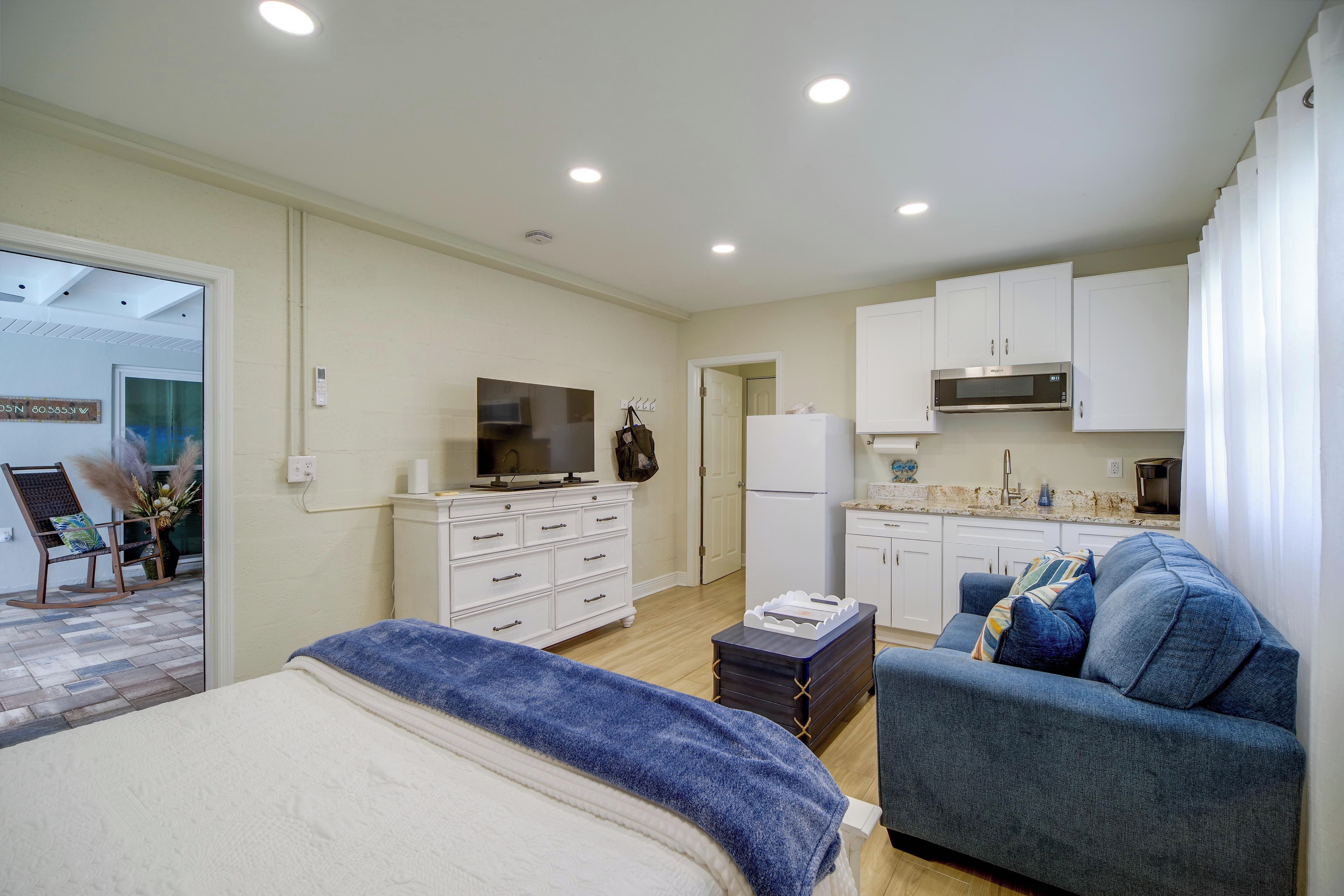 Un dormitorio moderno con cama, televisor, cómoda y kitchenette.
