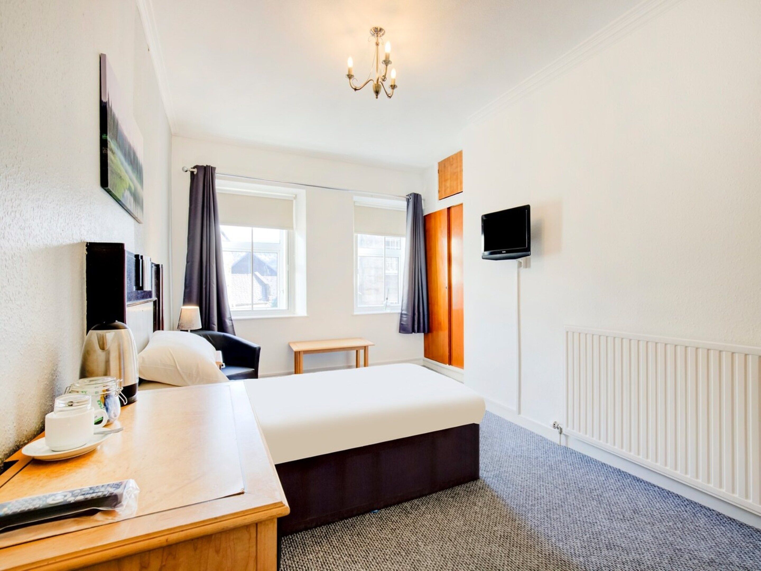 A hotel room with a bed, bedside table, TV, and a window with curtains.