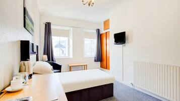 A hotel room with a bed, bedside table, TV, and a window with curtains.