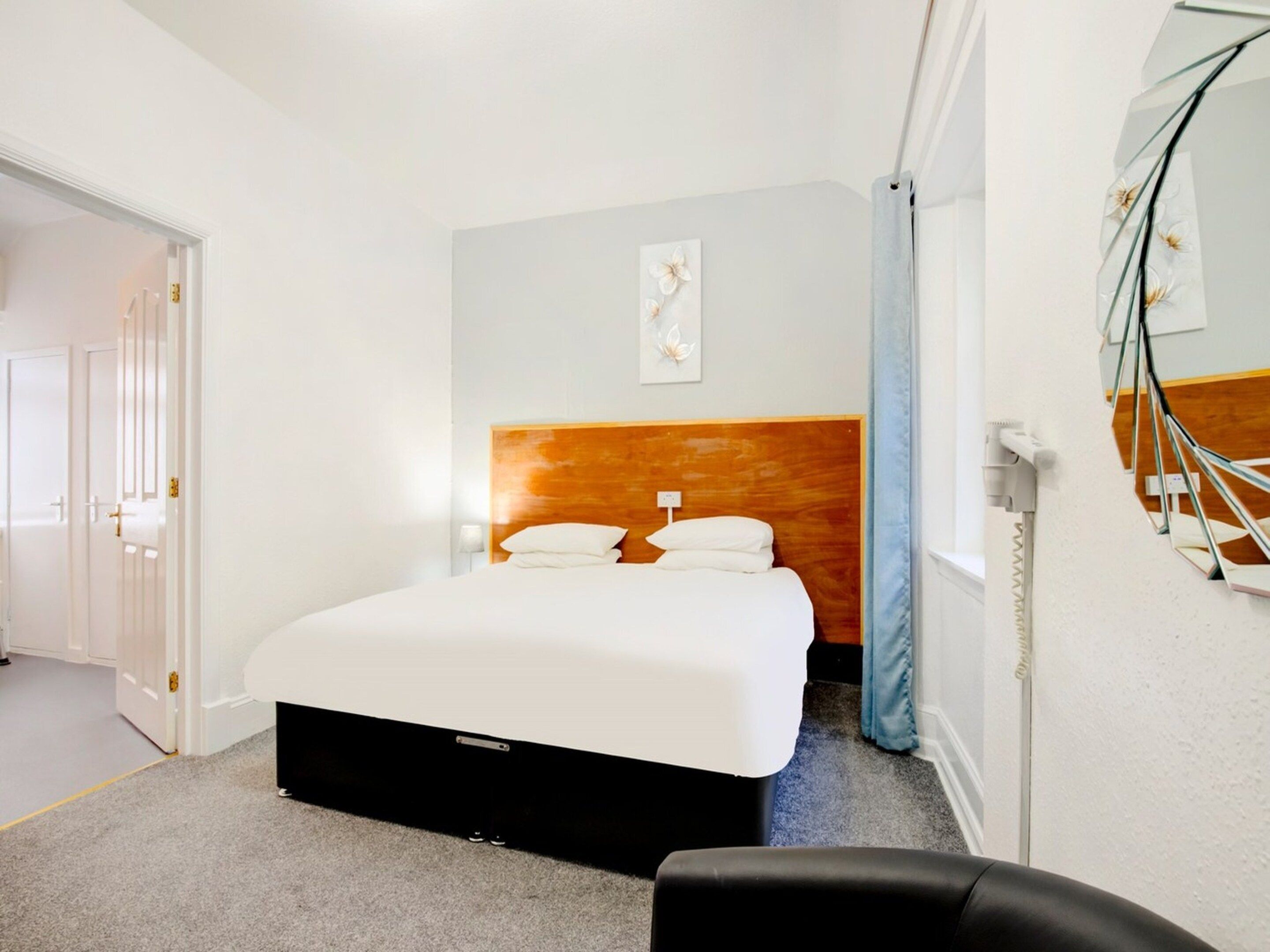A hotel room with a bed, a nightstand, a wall-mounted mirror, and a door.