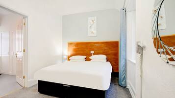 A hotel room with a bed, a nightstand, a wall-mounted mirror, and a door.