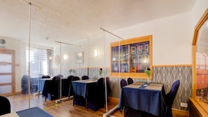 Un área de comedor con mesas dispuestas para huéspedes, un ventanal con vistas y una lámpara fijada a la pared.