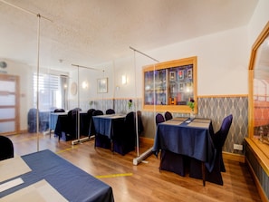A dining area with tables set for guests, a window with a view, and a wall-mounted light fixture. - Standard Double Room - Shared (Aberlour)