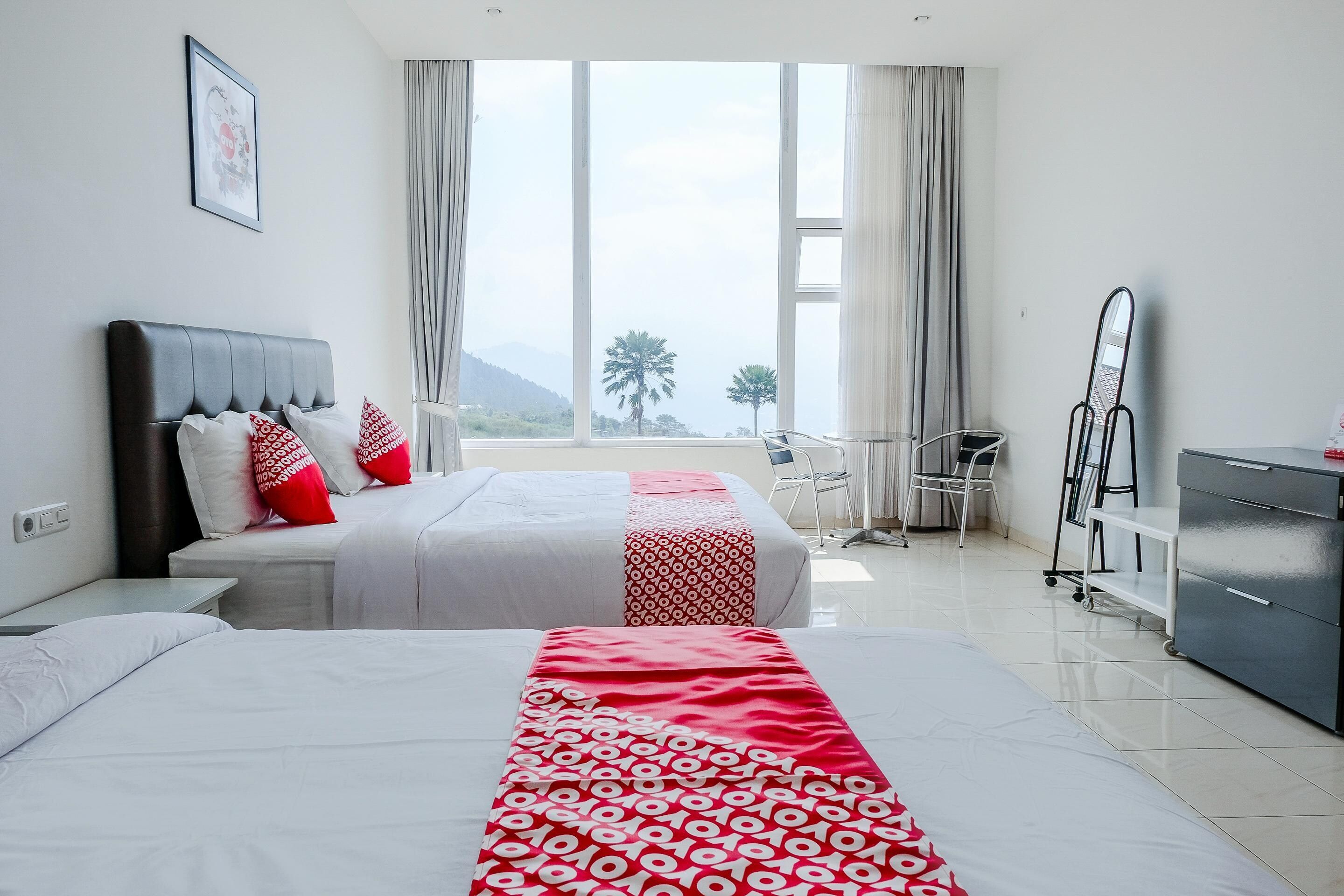 A hotel room with two beds, a desk, a chair, a dresser, and a large window with a view of the outdoors.