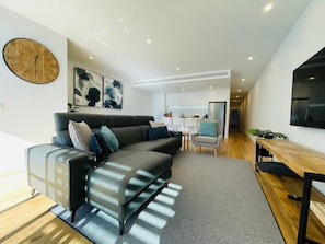 En moderne stue med en hjørnesofa, et spiseområde og et køkken i baggrunden.