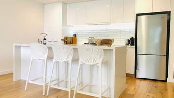 A modern kitchen with white cabinetry, a stainless steel refrigerator, and three white bar stools.