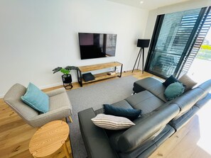 En moderne stue med sofa, sofabord, fjernsyn monteret på væggen og et gulv-til-loft-vindue.