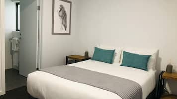 A bedroom with a bed, two bedside tables, a nightstand, a framed artwork, and a door leading to a bathroom.