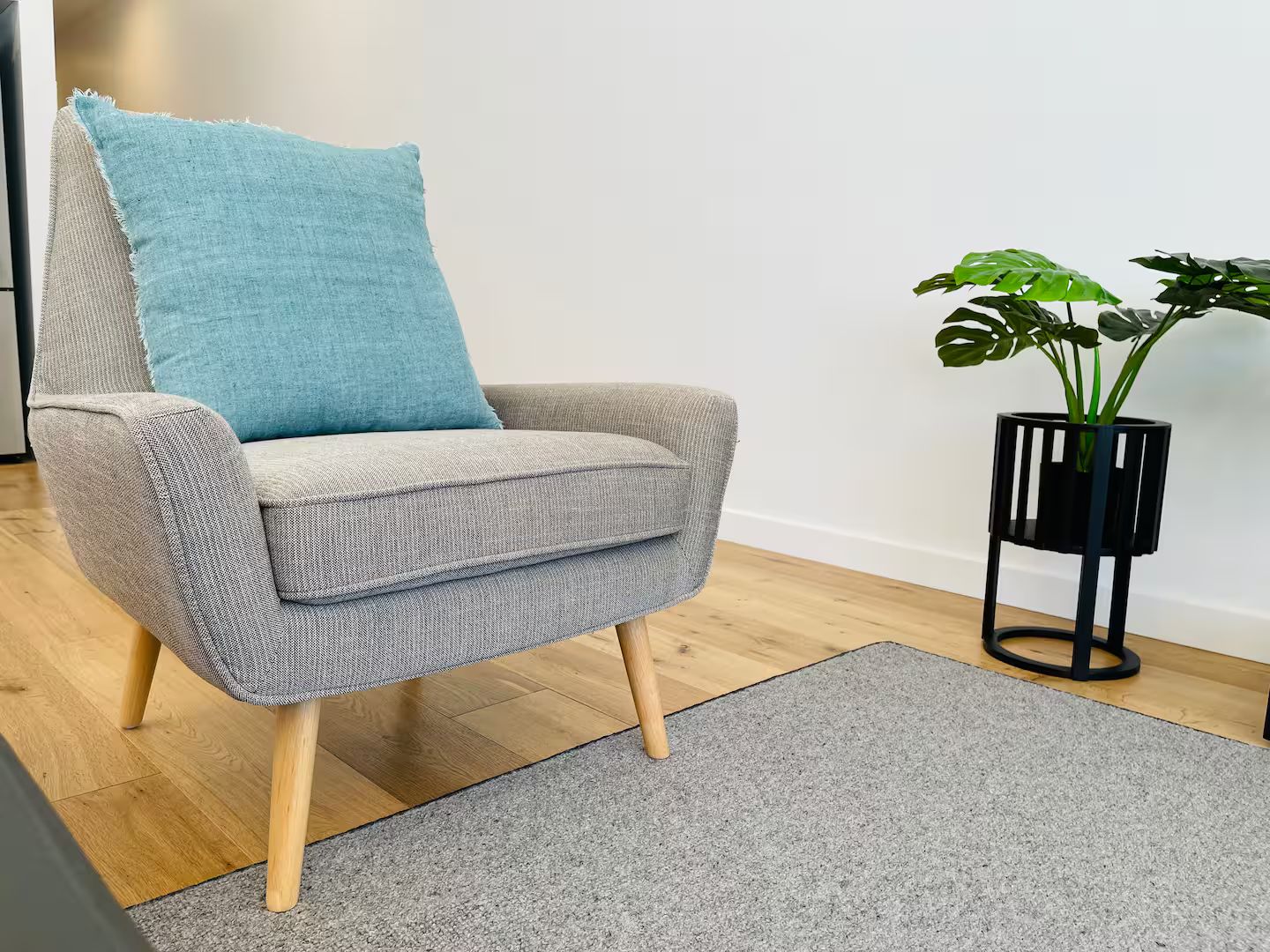 A grey armchair with wooden legs and a blue cushion, positioned on a grey rug.