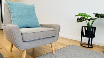 A grey armchair with wooden legs and a blue cushion, positioned on a grey rug.