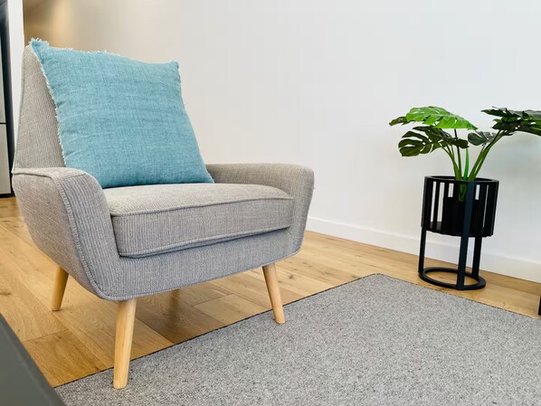 Un sillón gris con patas de madera y un cojín azul, sobre una alfombra gris.