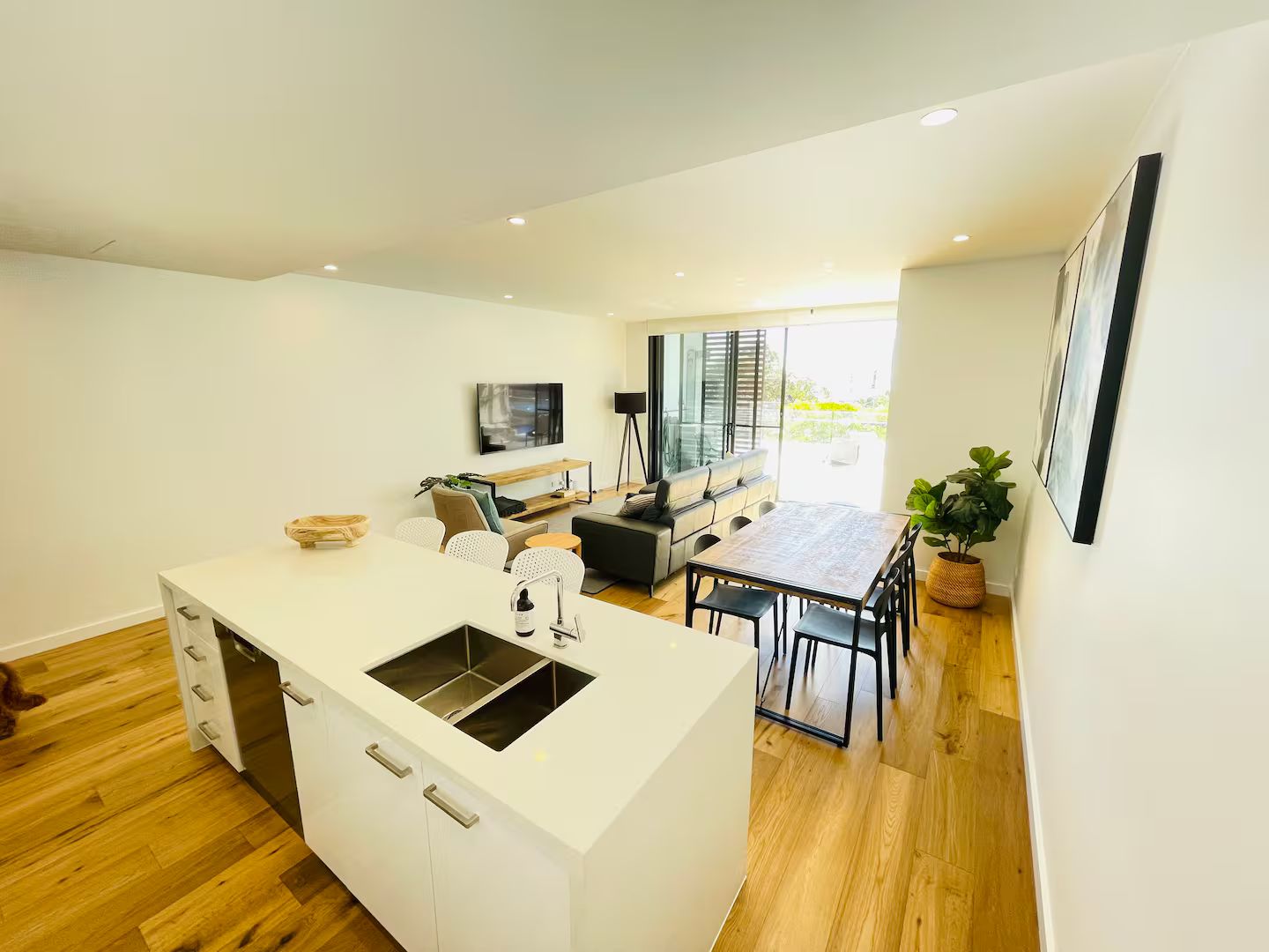 Een moderne keuken met een centraal eiland, een eetgedeelte met een tafel en stoelen, en een zithoek met een bank en een televisie.