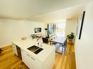 Una cocina moderna con una isla central, comedor con mesa y sillas, y zona de estar con sofá y televisor.