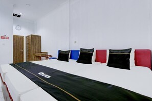 A hotel room with a large bed, a wooden wardrobe, a small table, and a clock on the wall. - Spacious Triple Suite for Groups With Free Wifi (Yogyakarta)