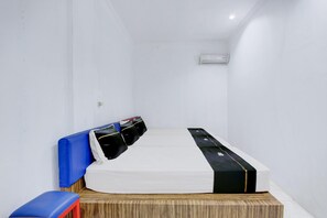 A small, narrow hotel room with a single bed, a small table, and a blue chair. - Spacious Triple Suite for Groups With Free Wifi (Yogyakarta)