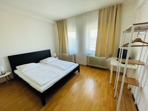 A hotel room with a double bed, a bedside table with a lamp, a radiator, a TV on a stand, and a clothing rack.